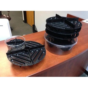 Two black perforated plastic components with circular grids stacked on a wooden desk.