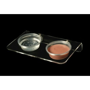 Two small round makeup containers on a clear acrylic tray, one with brown cream and the other empty.