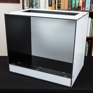 Empty white metal computer case with black interior on a desk; bookcase with colorful spines in the background.