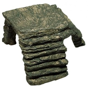 Rough, layered rock sculpture resembling a small chair with stone arms and a flat seat.