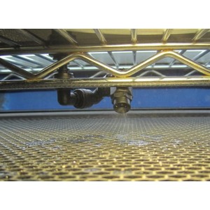 View under a perforated metal floor showing a pipe fitting and curved tubing.
