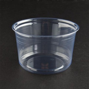 Clear disposable plastic cup on dark surface, empty and cylindrical with a rounded rim.