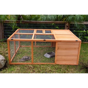 Wooden outdoor animal hutch with wire mesh sides, housing a tortoise on grass and a gray shelter inside.