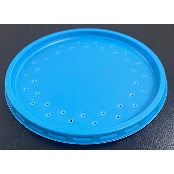 Blue circular lid with numerous small holes arranged around the edge, resting on a dark surface.